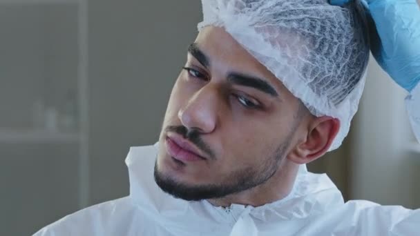 Portrait de épuisé fatigué jeune arabe médecin infirmier praticien en uniforme de protection gants en latex se tient à la clinique enlève casquette médicale de la tête expire avec soulagement après une dure journée de travail — Video