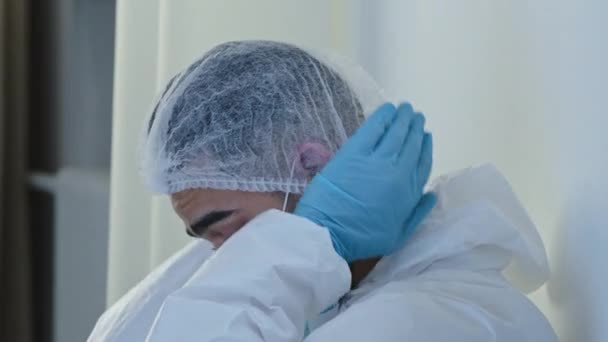 Side view unrecognizable male hero doctor nurse in medical protective uniform and blue mask on face sits in corridor of hospital clinic on floor feels tired exhaustion from fight against coronavirus — Stock Video