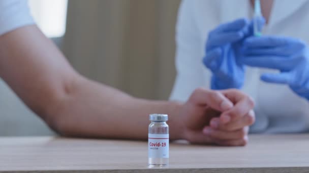 Close-up, bottle with covid-19 vaccine stands on table in hospital, female doctor hands hold syringe with coronavirus medicine preparing to give injection vaccination to unrecognizable male patient — Stock Video