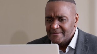 Üzgün, orta yaşlı, buruşuk, siyah Afrikalı iş adamı dizüstü bilgisayara bakıyor. İnternetten kötü haberler okuyor. E-posta reddediliyor.