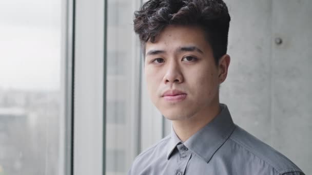 Portrét vážný mladý asijský chlap korejský japonec pracovník číňan obchod muž student dívá ven okno stojící v kanceláři vnitřní myšlení snění plánování při pohledu na kameru usmívající se zubatý — Stock video