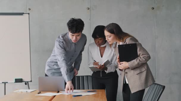 Multiethnic business team asijské muž, africká žena a běloška dívka kolegové manažeři diskutovat o projektu kontrola dat v dokumentech a v notebooku on-line servis stánek v moderní kancelářské společnosti týmová práce — Stock video