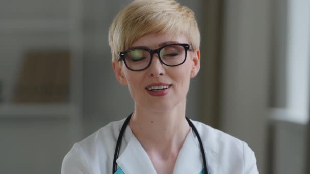 Portrait caucasian mature woman doctor female practitioner surgeon gynecologist lady with short hair wears glasses stethoscope and medical gown looking at camera talking on video call conference chat — Stock Video