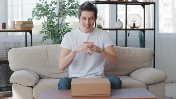 Homme caucasien adulte mâle client anniversaire gars assis sur canapé salon intérieur frotte paumes en prévision ouvre boîte en carton paquet cadeau peur peur horreur peur regarder à l'intérieur — Video