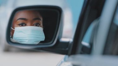 Araba aynasında yansıması güzel, Afro-Amerikan kadın sürücü, şık makyajlı siyah ırk kızı, araba tamirhanesinde oturan kadınların yüzüne tıbbi koruyucu maske takıyor.