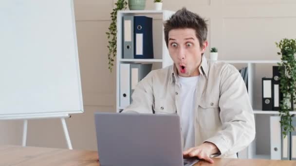 Masada oturan komik duygusal beyaz erkek serbest çalışan erkek dizüstü bilgisayarı açıyor. Şok edici bir sürpriz. Vay canına, iyi haberler alıyor. — Stok video