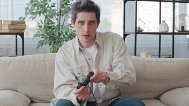 Καυκάσιοι ενήλικες χιλιετηρίδας 30 επικεντρώθηκε άνθρωπος άντρας gamer τύπος κάθεται στο σπίτι στον καναπέ στο εσωτερικό του σαλονιού απολαμβάνοντας ανταγωνισμό video game playing console controllers χειριστήριο joystick παιχνίδι — Αρχείο Βίντεο