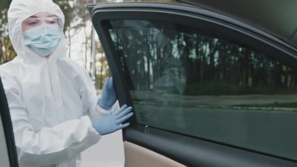 Внутренний вид автомобиля женщина медик лабораторный водитель курьер лаборатории в защитной медицинской одежде латексные перчатки и маска для лица открывает дверь автомобиля получения колеса привода, вождение во время вирусной пандемии — стоковое видео