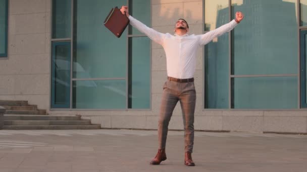 Pomyślny szczęśliwy szczęśliwy arabski hiszpański biznesmen szef szef lider przedsiębiorca z walizką stojących na zewnątrz w pobliżu nowoczesnej firmy budynku wygrywa dostaje szansę nowa praca sprawia, że gest zwycięstwa — Wideo stockowe