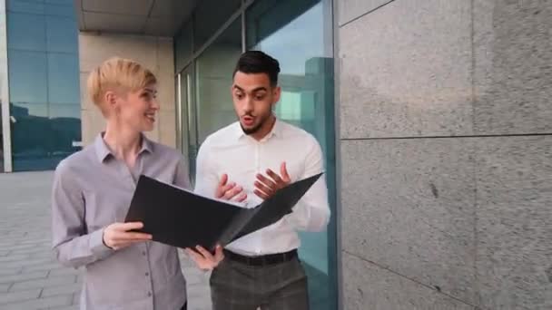 Przenoszenie materiału kaukaska kobieta szef lider doradca sekretarz pokazując folder z dokumentami do kolegi biznesowego mężczyzna dwa wielorasowe współpracownicy chodzenie na zewnątrz ulicy raduje uśmiech szczęśliwy z papierami — Wideo stockowe