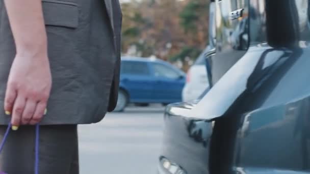 Femme caucasienne méconnaissable acheteur consommateur marche dans la rue à l'extérieur tient sac en carton violet dans l'achat de la main ouvre tronc de voiture de luxe chargements automobiles produit dans le concept de magasinage automobile — Video