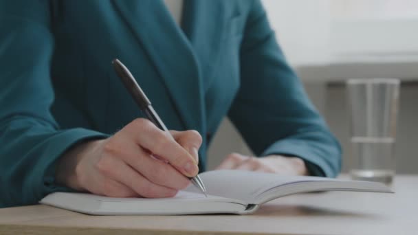 Close-up vrouwelijke handen, blanke vrouw in groene jas zittend aan bureau pen notities maken in dagboek. Onherkenbare zakenvrouw schrijft zakelijke ideeën en plannen in notebook om lijstschema te doen — Stockvideo