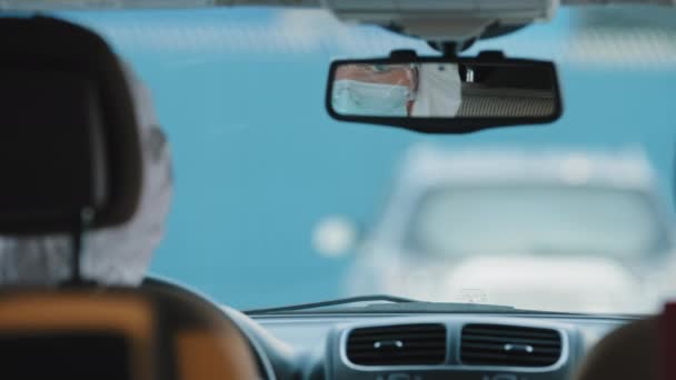 Bekijk van achteren binnen auto interieur vrouw arts laboratorium werknemer draagt beschermende medische pak kleding latex handschoenen zitten in auto kijkt naar reflectie in spiegel corrigeren transparante bril — Stockvideo