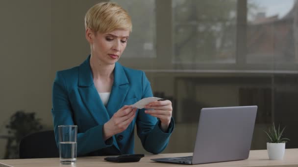 Sorprendido preocupado frustrado de mediana edad mujer caucásica empresaria lleva chaqueta verde sentado en la oficina en la mesa con el ordenador portátil mirando pago cheque enojado tira lejos la sensación de furioso — Vídeo de stock