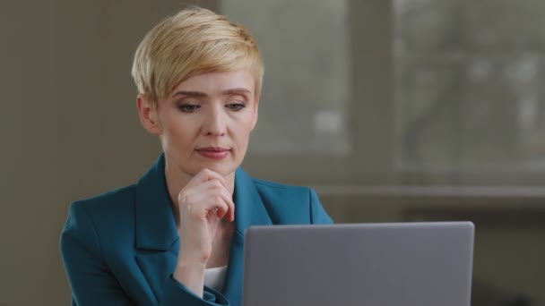 Pensive woman writer journalist business lady with short haired middle-aged female secretary sitting at table in office looks at laptop thinks idea strategy plan holds chin with hand deep in thoughts — Stock Video