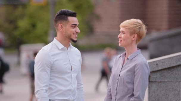 Two friendly multiracial colleagues arabic spaniard hispanic man and caucasian woman business co-workers stand outdoors in street talking discussing conversation dialogue negotiations about project — Stock Video