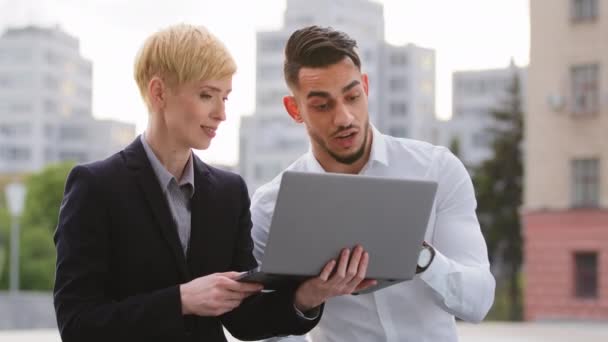 Glada multietnisk multiracial par kollegor arabiska latinamerikanska man och kaukasiska kvinna står nära business center på gatan utomhus och arbetar på laptop diskutera projekt analysera data lagarbete — Stockvideo