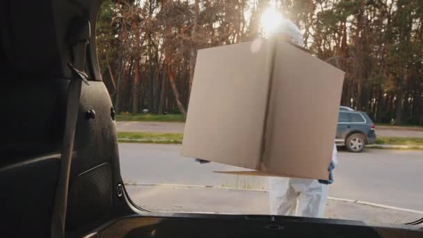 Woman doctor nurse medical worker courier buyer consumer wears protective suit mask and goggles from coronavirus puts large cardboard boxes parcel with orders in trunk of car, delivery during pandemic — Stock Video