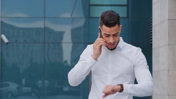 Ritratto di successo grave arabo ispanico uomo d'affari spagnolo capo leader indossa camicia bianca formale si erge all'aperto parla cellulare risponde chiamata guarda i controlli orologio da polso in ritardo — Video Stock