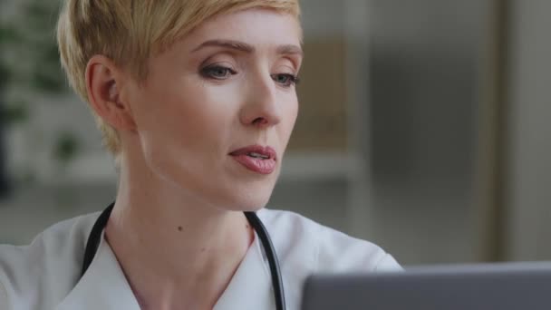 Portret kobiety twarzy ze stylowym makijażem dojrzały biały 40 kobieta lekarz lekarz praktykuje nosi biały płaszcz i stetoskop mówi w laptopie kamera internetowa konsultuje online wideokonferencji czat zdalnie — Wideo stockowe
