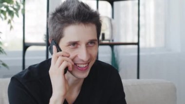 Siyah tişört giyen, beyaz tenli erkek portresi. Cep telefonuna duygusal olarak cevap veren, cep telefonuyla konuşan, cep telefonuyla gülümseyen, hava öpücüğüyle son konuşmayı yapan.