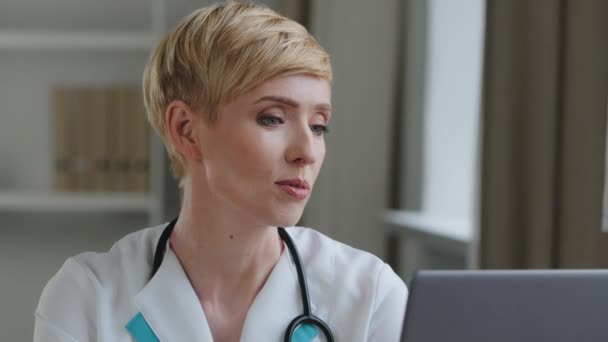 Portré rövid hajú középkorú 40-es éveiben orvos nő szakorvos visel fehér orvosi kabát sztetoszkóp beszél keres laptop kamera online konzultáció videó hívás konferencia chat — Stock videók