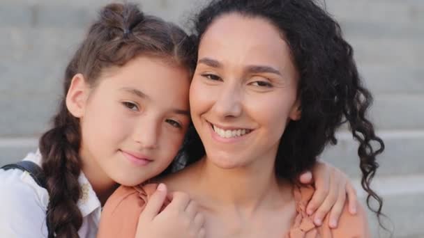 Retrato hispano familia morena joven madre maestra niñera mamá y pequeña linda niña niña pequeña colegiala alumno hija niño abrazo abrazo abrazo abrazo abrazo mirando a la cámara al aire libre — Vídeo de stock