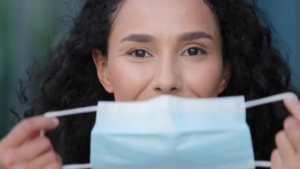 Retrato al aire libre mujer hispana joven mujer mujer pone en la cara máscara médica protectora que protege la salud de la infección por coronavirus covid muestra como pone pulgares hacia arriba recomienda usar respirador — Vídeos de Stock