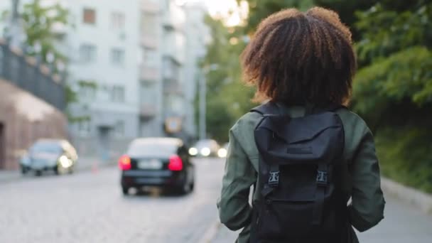 Sırt çantalı kıvırcık saçlı turist kız büyük şehirde yol boyunca gezip fotoğraf çekiyor. Genç kadın fotoğrafçı blogcu gezi sırasında profesyonel kamera kullanarak fotoğraf çekiyor. — Stok video