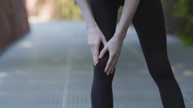Tanımlanamayan zayıf atletik kadın siyah taytlı bayan koşucu koşucu koşucu sporcu parkta koşarken dizinden sakatlanmış vücut durumu, eklem ağrısı, eklem ağrısı sorunu.