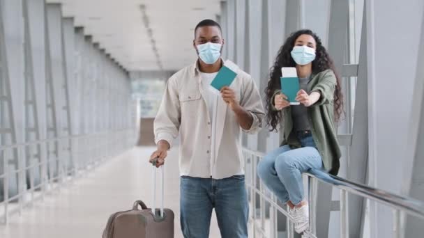 Çantalı mutlu çok ırklı çift İspanyol kadın ve Afro-Amerikan erkek koca havaalanında yüzlerini koruyan maskeler takıp dans ederken pasaportlarını ve uçak biletlerini gösteriyorlar. — Stok video