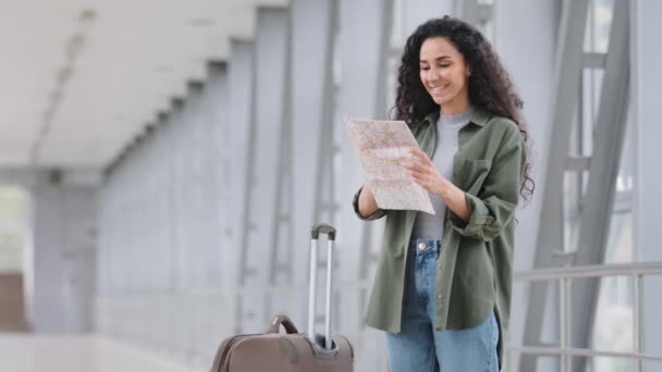 Ensam glad ung latinamerikansk vacker vaccinerad kvinna kvinnlig turist resenär står i flygplatsterminalen i järnvägsstationen med resväska tittar på kartan söker resväg slutet av karantän — Stockvideo