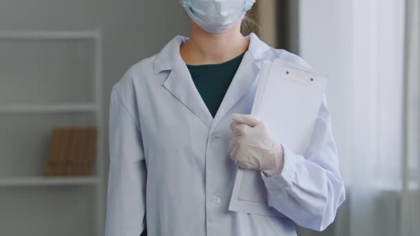 Close-up unrecognizable woman nurse doctor medical worker practitioner surgeon wears white coat face mask and latex gloves stands in hospital holds folder with documents papers diagnoses prescriptions — Stock Video