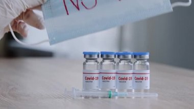 Dört şişe ahşap masa ve dört şişe kovan aşısı Coronavirus ilacı pandemik ilaç şırınga kadın eli lateks eldivenli koruyucu maske ve aşı yok.