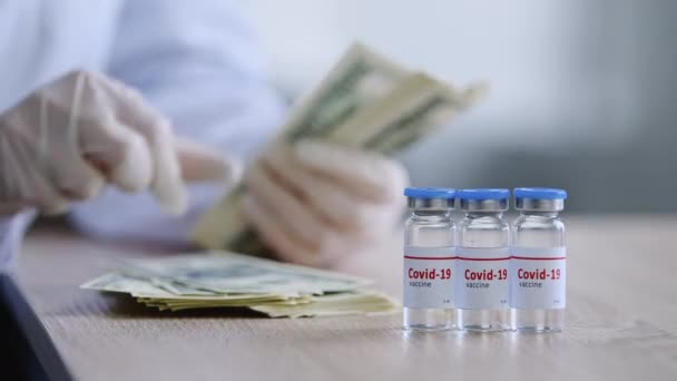 Close-up three bottles with coronavirus vaccine drug cure for covid stands on table female hands of scientist pharmacist doctor in latex gloves hold money counting dollars banknotes cash salary saving — Stock Video