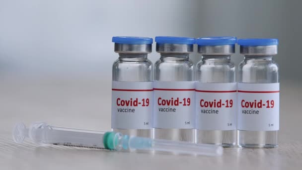 Close-up van vier glazen flessen met vaccin tegen covid-19 virus remedie tegen epidemie van coronavirus immunisatie staan op houten tafel in laboratorium ziekenhuis in de buurt van spuit, vaccinatie concept — Stockvideo