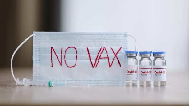 Detailní průhledné skleněné lahvičky s tekutou vakcínou anti-covid-19 koronavirus na stole poblíž injekční stříkačky a lékařské masky s nápisem žádné očkování, odmítá imunizaci během pandemie — Stock video