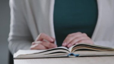 Yakından tanınmayan bir kız öğrenci üniversitede oturmuş ders çalışıyor, ders kitabı okuyor, beyaz kadın öğretmen ellerinin sayfası ev romanı okuyor.