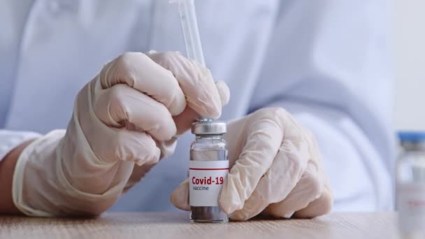 Κοντινό πλάνο γυναίκες γιατροί χέρια σε ιατρικά γάντια λατέξ κρατώντας σύριγγα με φάρμακο στο παρασκήνιο του λευκού παλτό. Ampoule με εμβόλιο για covid-19 θεραπεία θεραπεία για coronavirus κερδίζοντας υγρό αντιβιοτικό — Αρχείο Βίντεο