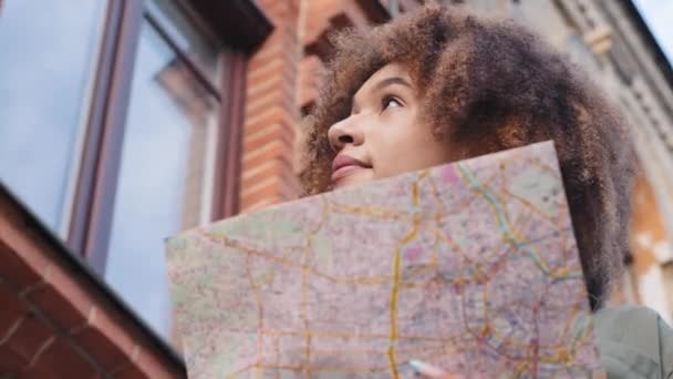 Fiatal vonzó afro-amerikai fekete nő turista papír térkép séták központjában a város nyári napsütéses napon, látvány látnivalók, modern építészet, körülnéz, használja útikönyv városnézés — Stock videók