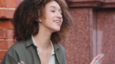 Sakin, Afro-Amerikan bir kadın, kulaklık takmış, gözleri kapalı dışarıda oturuyor. Serene happy millennial girl listen cool music or modern sound, dance, fun days or weekend
