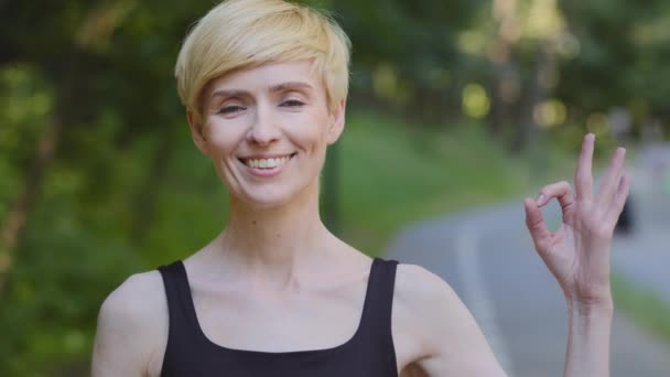 Portrait extérieur femme athlète femme coureuse caucasienne d'âge moyen dame debout dans le parc extérieur près de l'arbre vert montrant ok geste ok signe symbole de satisfaction tout beau regarder la caméra — Video