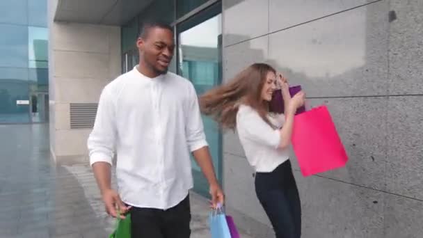 Pareja multiracial afroamericana afro hombre y mujer caucásica marido y mujer novio y novia caminando al aire libre desde la tienda del centro comercial con bolsas de compras compras bailando feliz con descuentos — Vídeos de Stock