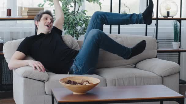 Kaukaski młody mężczyzna millennial facet nosi czarny t-shirt i dżinsy spada leżeć na miękkiej wygodnej kanapie korzystając relaks po ciężkim dniu w pracy sprawia, że przerwa na kanapie w przytulnym salonie — Wideo stockowe