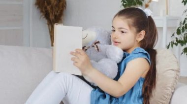 Kafkas asıllı İspanyol liseli kız çocuk öğrenci evdeki kanepede oturuyor iç tarafta beyaz ayıcığa sarılıyor içeride edebiyat dersleri okumaktan keyif alıyor.