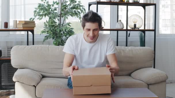 Kaukasische millennial erwachsener Mann Käufer Verbraucher erhält Paket sitzt auf Couch öffnenden Karton Geschenk Produkt Überraschung von Online-Shop fühlt Angst Angst Angst versteckt sich hinter Sofa mit Schrecken — Stockvideo