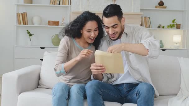 Español hispano casado pareja étnica familia sentarse en sofá en casa recibir carta documento por correo aviso de banco con buenas noticias leer papel ganar lotería dinero regocijarse celebrar gritar con felicidad — Vídeo de stock