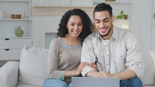 Español árabe pareja casada cónyuges hombre y mujer marido y esposa novio y novia sentado en el sofá haciendo video llamada conferencia charlando en el ordenador portátil webcam videocalling desde casa de forma remota — Vídeos de Stock