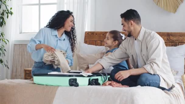 多民族家庭多种族的年轻父母带着小女儿坐在床上收拾行李聊天准备出国度假 — 图库视频影像