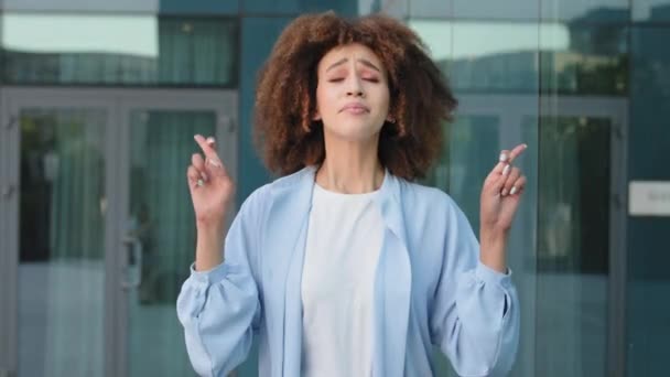 Εξωτερικά πορτρέτο γυναίκα ελπιδοφόρα κυρία της Αφρικής Αμερικανός κορίτσι afro γυναίκα στέκεται στην πόλη κτίριο φόντο σταυρώνει τα δάχτυλα ζητά από το Θεό για την τύχη ελπίζει να προσευχηθούν αναδίπλωση παλάμες κάνει ευχή με κλειστά μάτια — Αρχείο Βίντεο